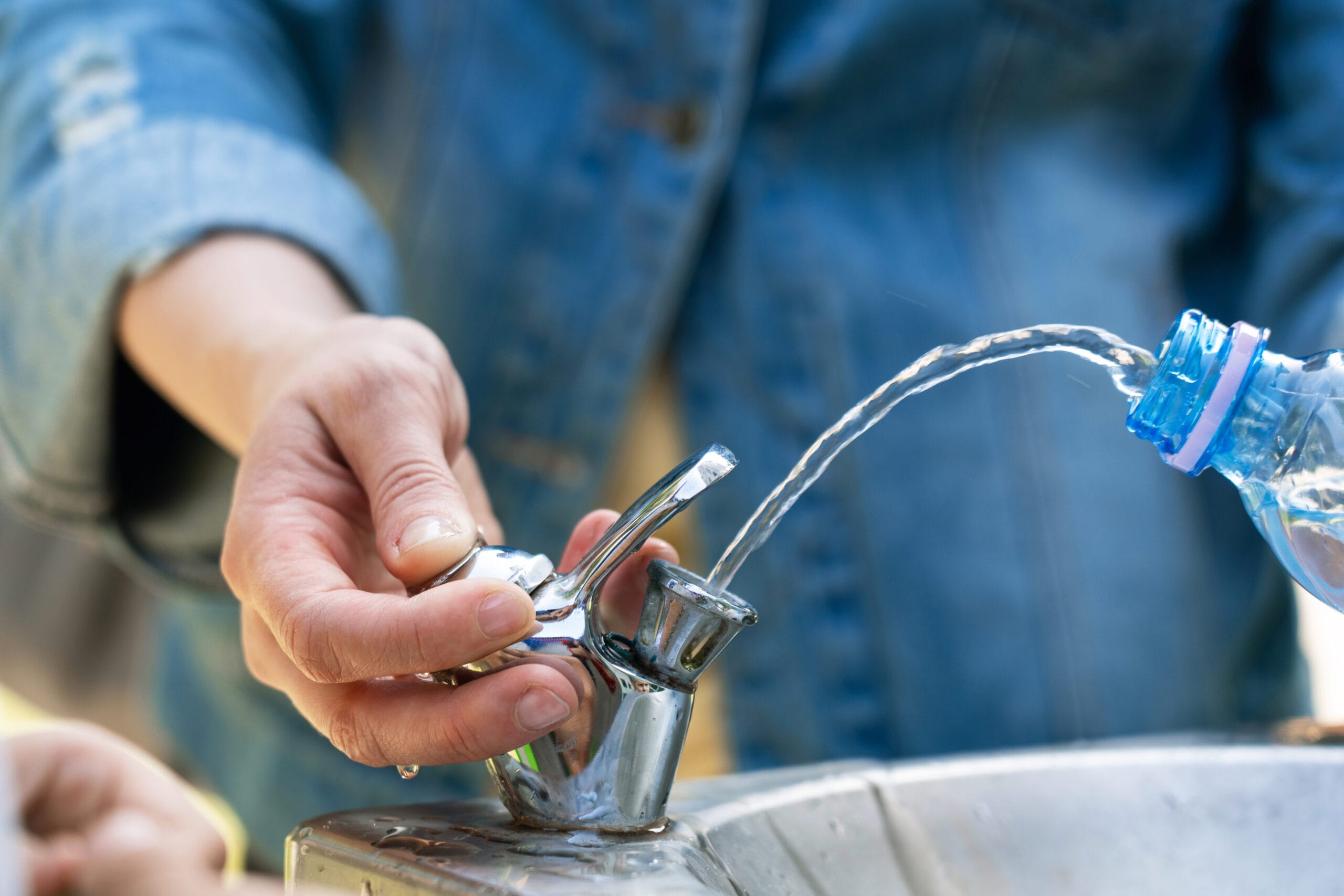 Filling a water fountain with water from a plastic bottle while holding the fountain's tap