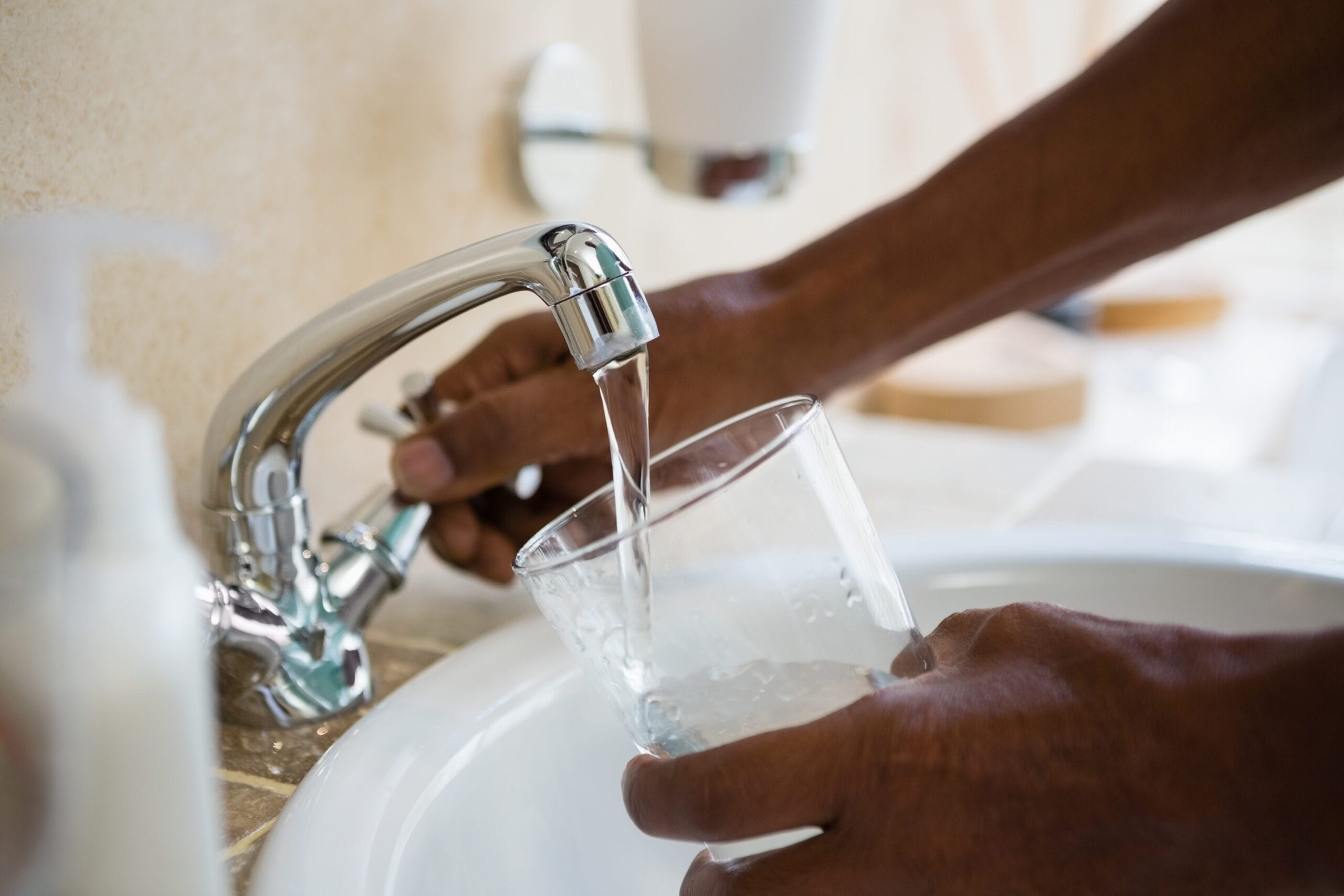Person filling a glass with water from a bathroom sink faucet
