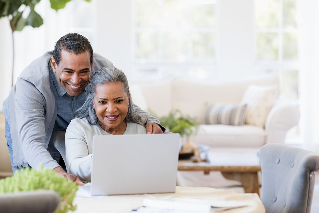 Older couple smiling and using a laptop together in a bright living room
